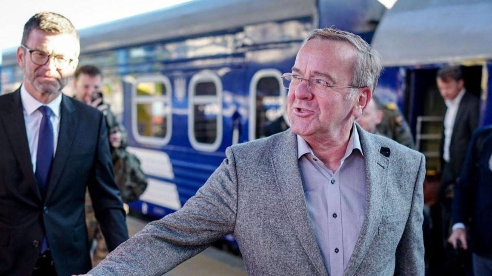 Boris Pistorius, German Defense Minister, wearing a gray suit jacket and glasses, smiles as he exits a train in Kyiv. Accompanied by staff.