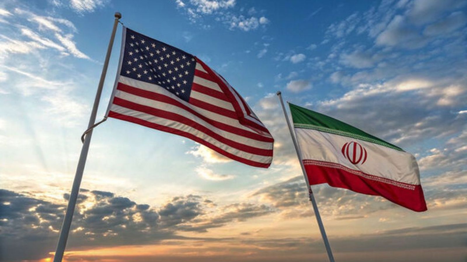 The national flag of the United States of America (left) and the national flag of Iran (right) on flagpoles during sunset.
