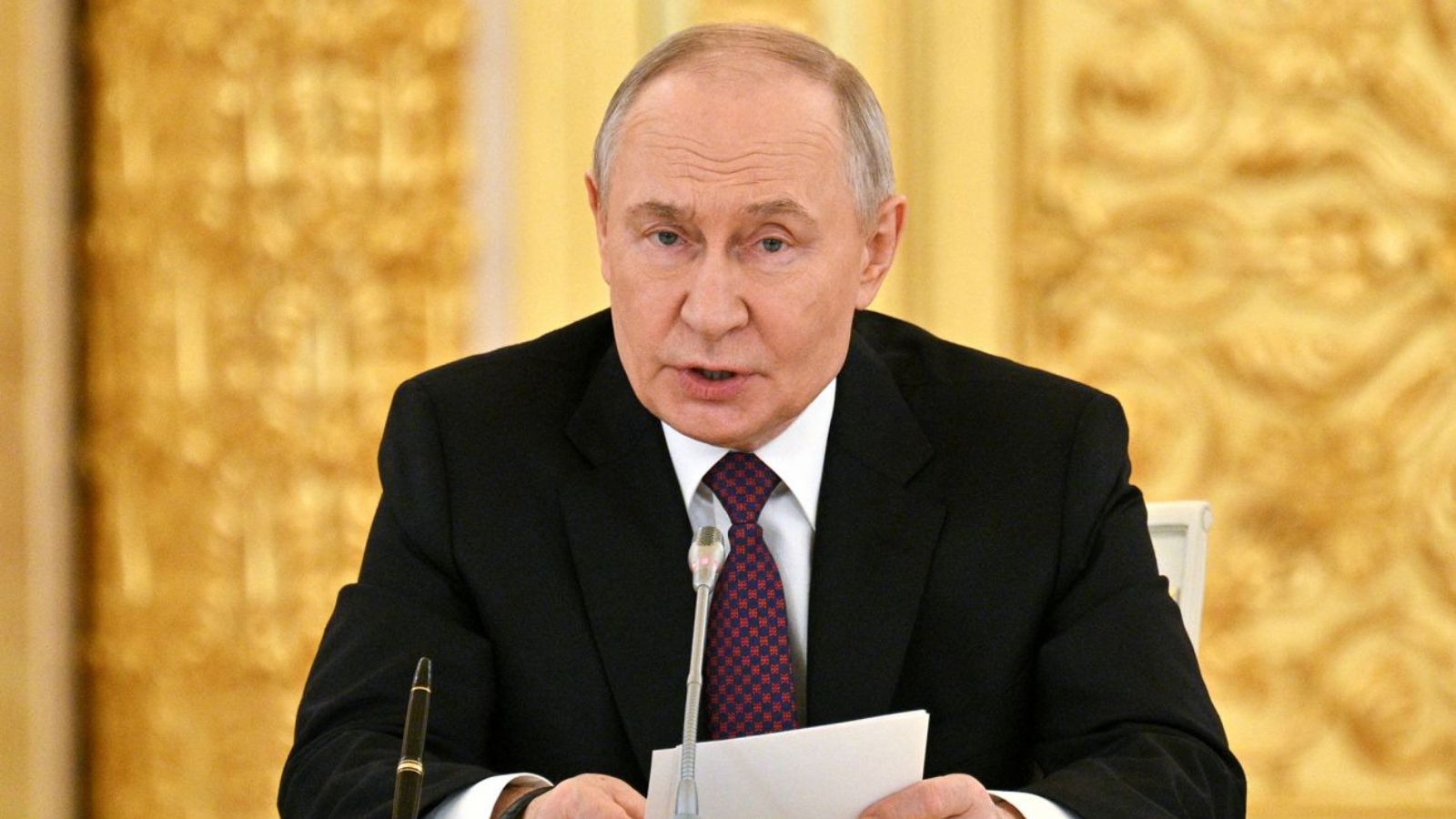 Vladimir Putin sitting at a desk during an official press conference in the Kremlin.