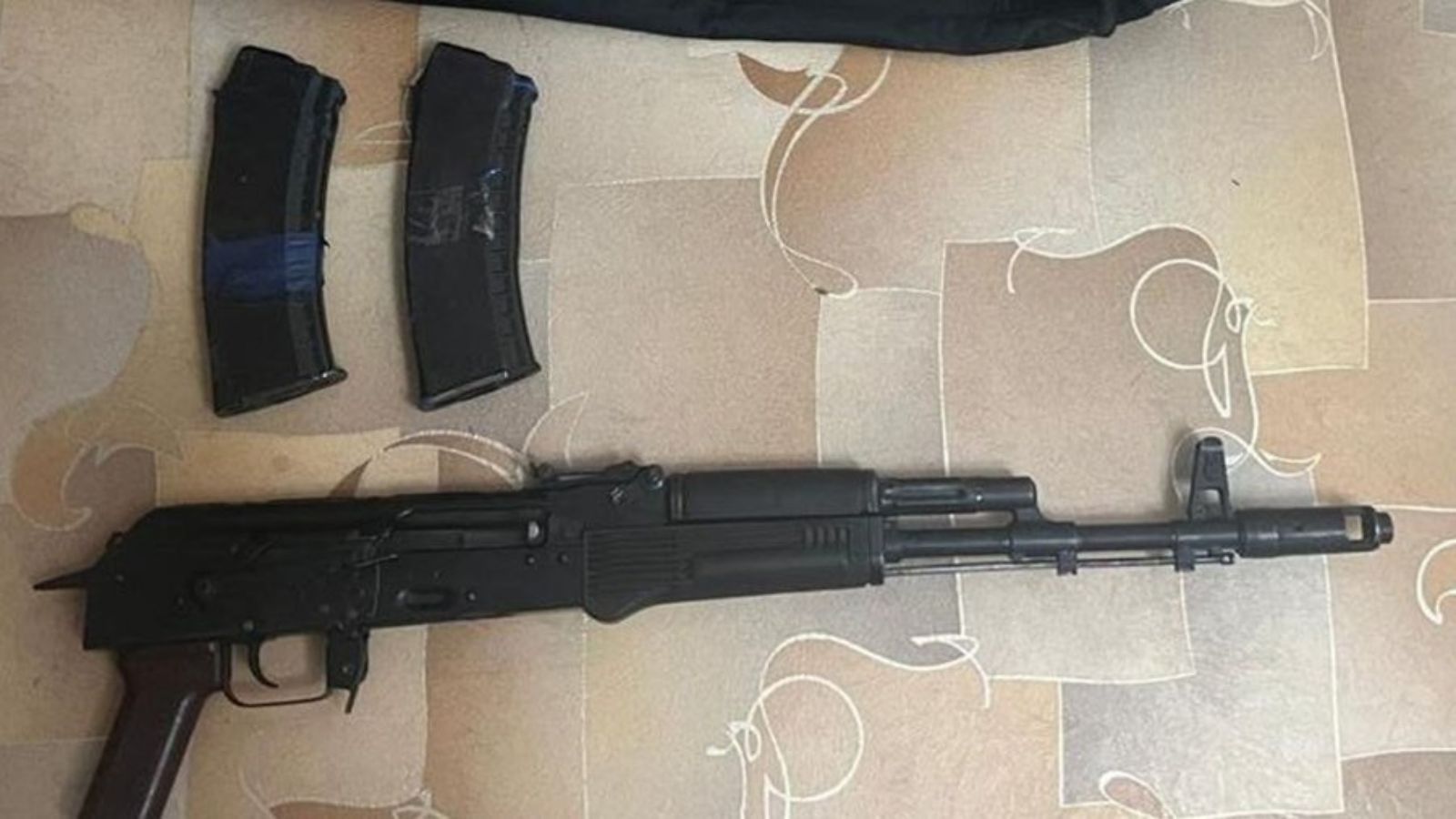 An AK-74 assault rifle and two loaded magazines laid out on the floor.